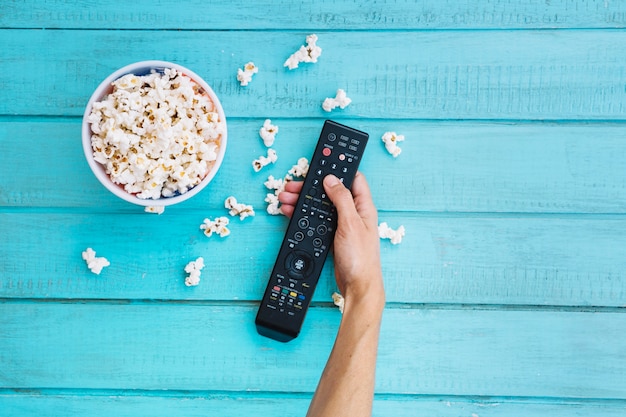 Person holding remote control near popcorn bucket