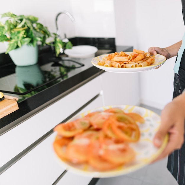 A person holding slices of tomato and delicious pasta on plate