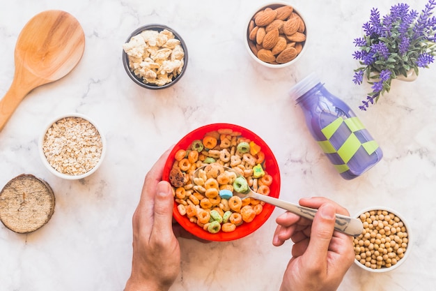 Person holding spoon with cereal above red bowl