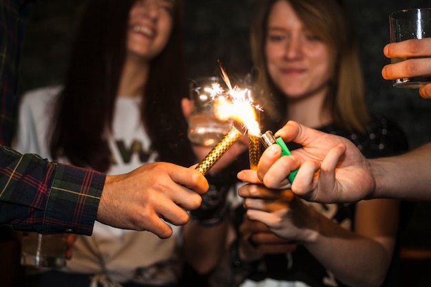 Free photo a person lighting sparkle candle with cigarette lighter with friends