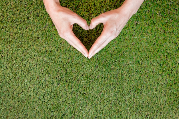 Free photo person making a heart with his hands on grass with copy space