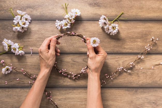 A person making wreath with white flower and twigs on wooden table