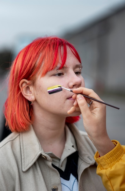 Person painting a non binary flag on a friend outside