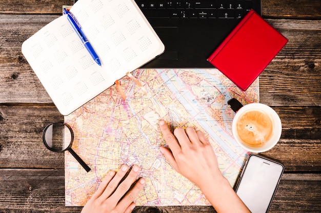 Free photo person pointing at destination on map with cup of coffee and diary on table