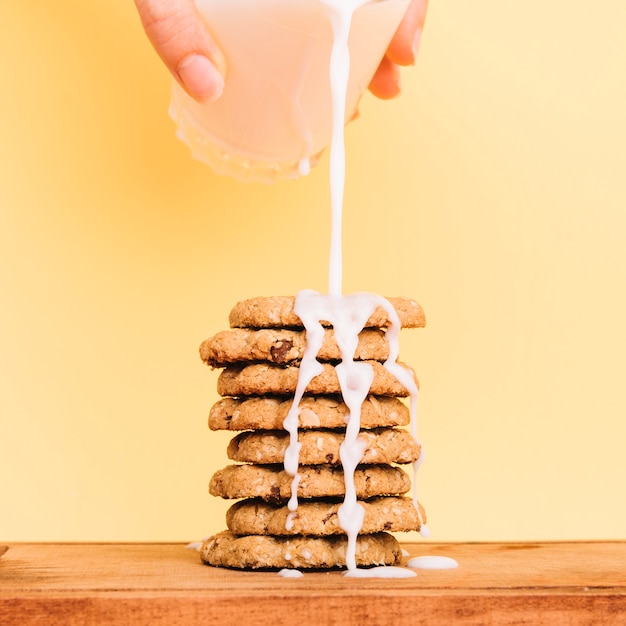 Free photo person pouring milk from glass on cookies stack