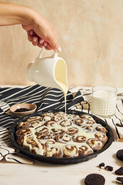 Person pouring the white cream on the delicious cinnamon rolls