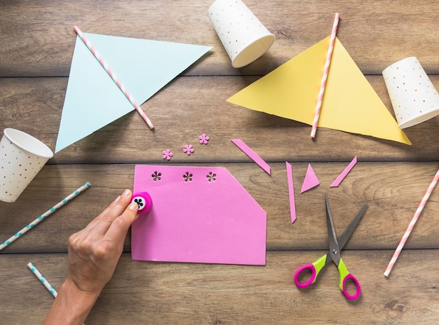 Free photo a person punching floral design on pink paper over the table