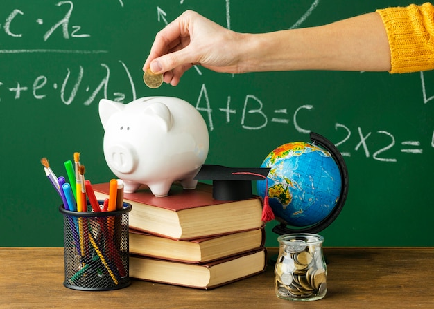 Person putting coins in piggy bank with books and pencils