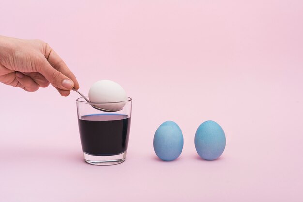 Person putting spoon with egg into glass with paint 