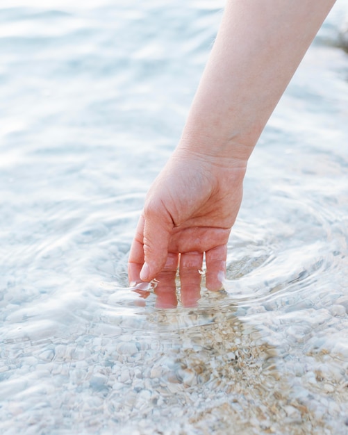 Free Photo person putting their hands in clear water with sand