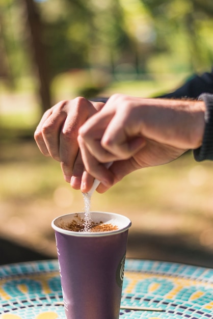 A person's hand adding sugar in the take away coffee cup at outdoors