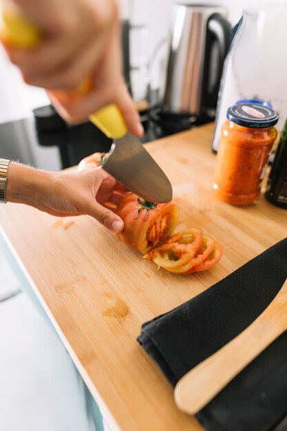 A person's hand cutting slices of tomato with sharp knife