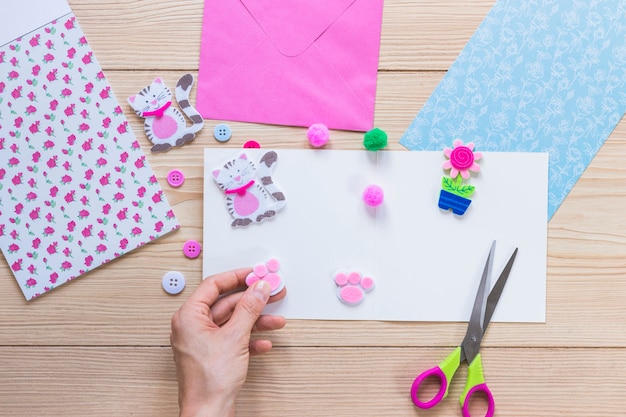 A person's hand decorating sticker on white paper over the wooden table