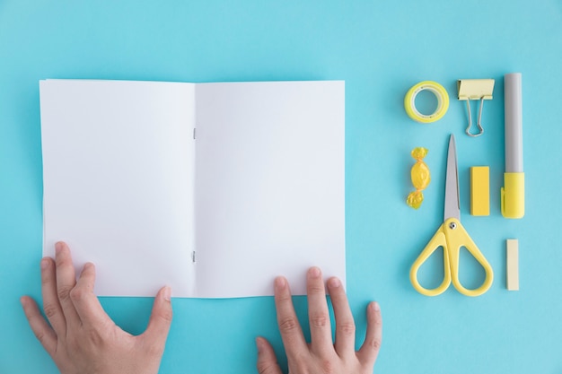 Free photo a person's hand holding blank page with stationery and candy on blue backdrop