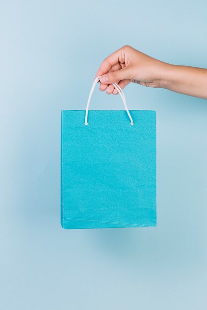 A person's hand holding blue paper shopping bag