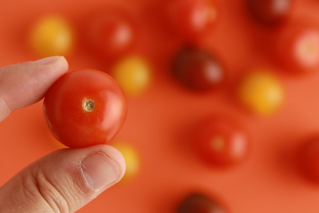 Free photo person's hand holding a cherry tomato on a blurred background