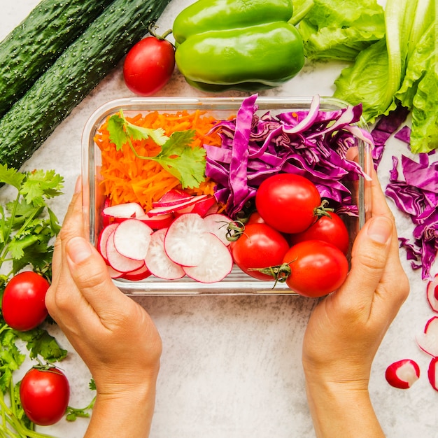 Free photo person's hand holding fresh vegetables and ingredients for salad in container