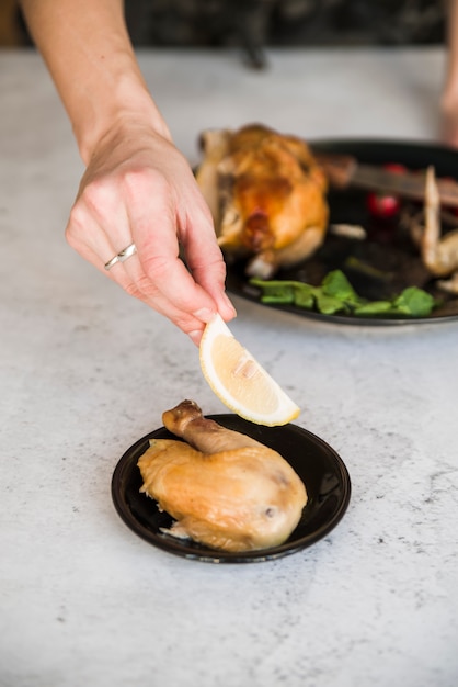 Free photo person's hand holding lemon slice near roasted chicken leg