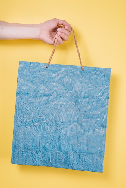 Free Photo a person's hand holding shopping bag against yellow background