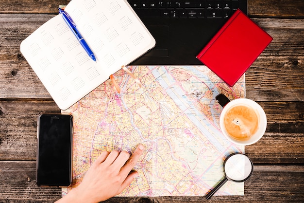 Free Photo person's hand pointing at location on map with coffee and smartphone on table