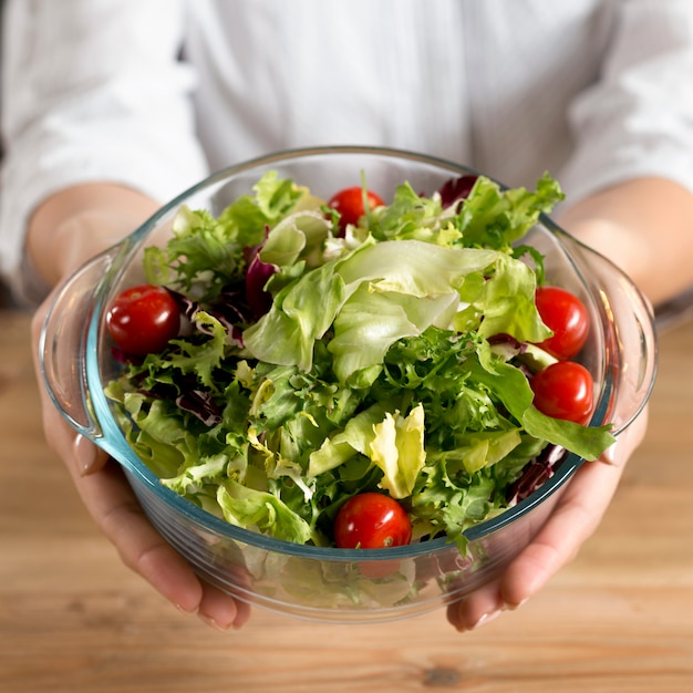 Free photo person's hand showing green leafy vegetable salad with red cherry tomatoes