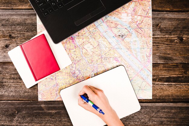 Person's hand writing on notepad with diary and map on wooden table