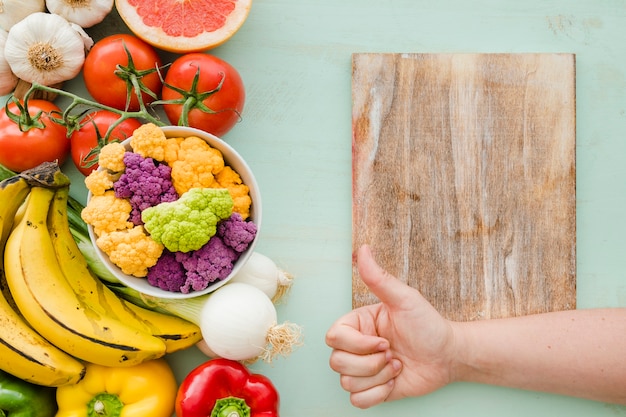 Free photo a person showing thumbsup sign over the chopping table and fresh healthy food