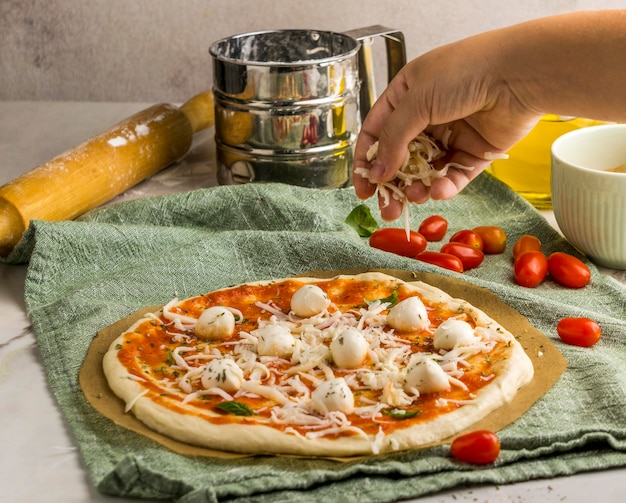 Free photo person sprinkling mozzarella cheese on pizza