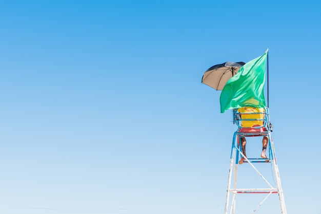 Free photo person standing on the security seat at the beach with a waving green flag