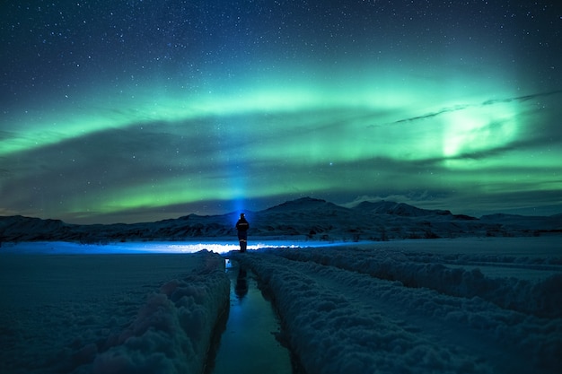 Person standing on snow covered ground under green sky