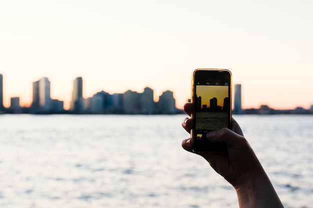 Free photo person taking photo of city sunset on smartphone