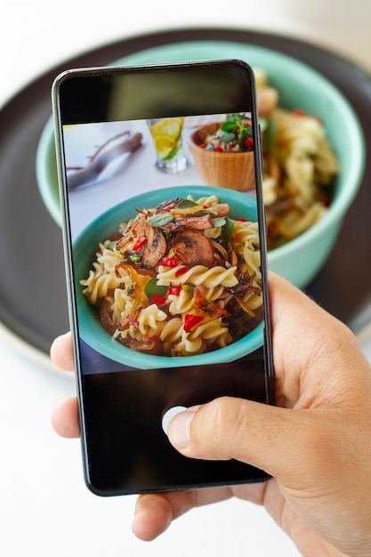 Free Photo person taking photo of pasta bowl with smartphone