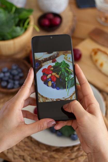 Free photo person taking photo of plate of tomatoes, blueberries and spinach with smartphone