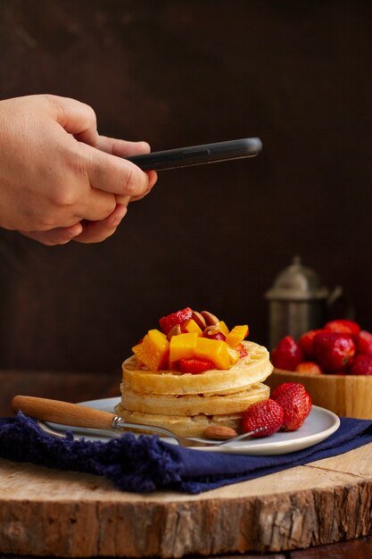 Person taking photo of waffles and strawberries with smartphone