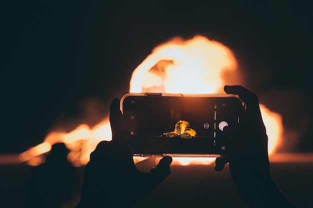 Free Photo person taking a picture of the bonfire with a smartphone at night time