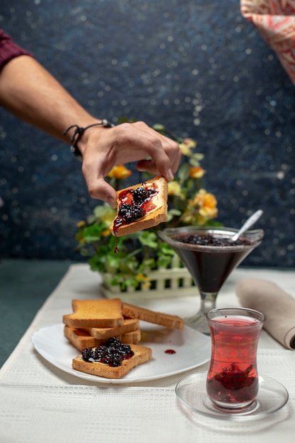 Free photo a person taking a toast with jam. a glass of black tea around.