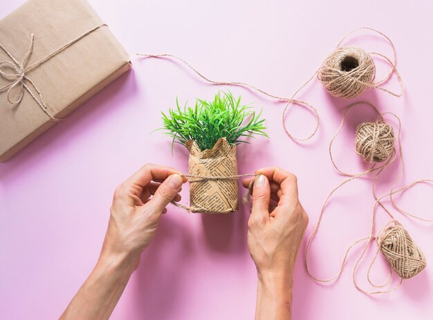 A person tying fake grass bundle with string on pink background