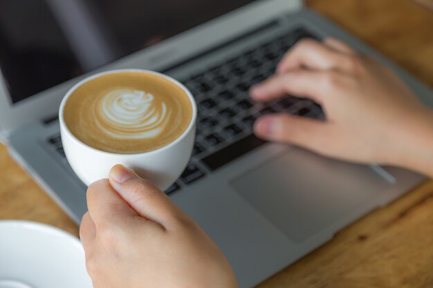 Person typing on a laptop holding a cup of coffee