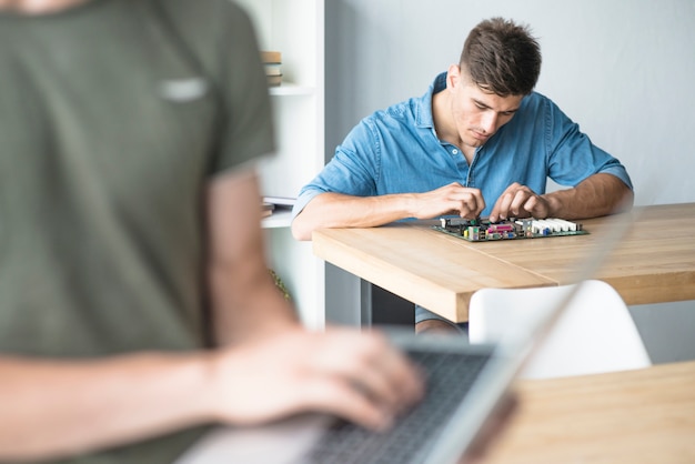 Free photo a person using laptop with man repairing motherboard at background