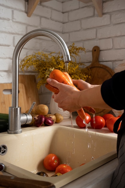 Free photo person washing carrots in the kitchen