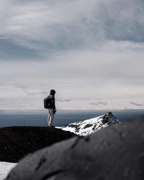 A person wearing backpack standing at the top of a mountain under cloudy sky