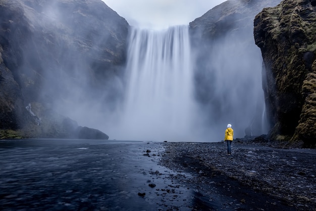 Free photo person wearing a yellow jacket standing at the mesmerizing waterfall