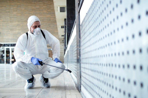 Person in white chemical protection suit doing disinfection of public areas to stop spreading highly contagious corona virus