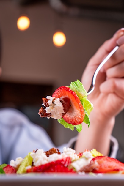 Person with a fork holding some of the salad made of fruits and vegetables