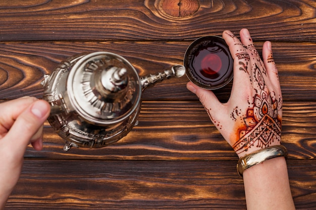 Person with mehndi pouring tea into small cup