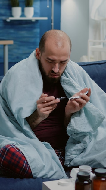 Free Photo person with sickness looking at tablets of capsules to cure disease and virus symptoms. man with cold and flu holding medication and pills for healthcare treatment. ill adult with drugs