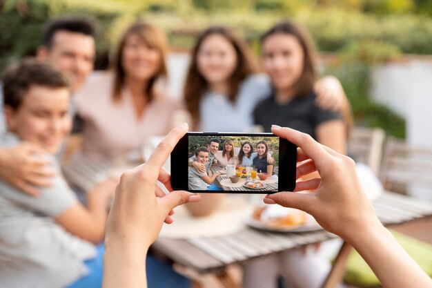 Person with smartphone taking photo of family having lunch outdoors together