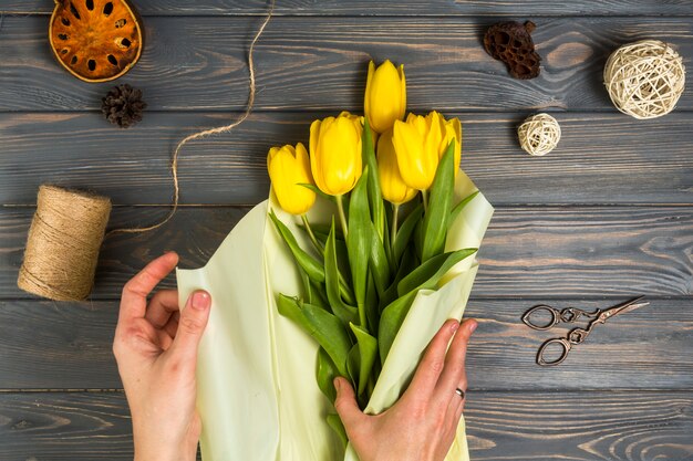 Free photo person wrapping yellow tulips in pack paper