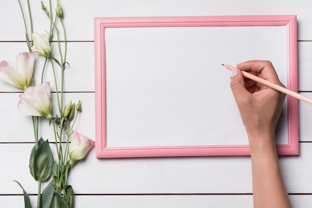 Free photo a person writing on blank white board with pencil against wooden backdrop