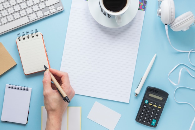 Free photo a person writing on notepad with pen on office blue desk